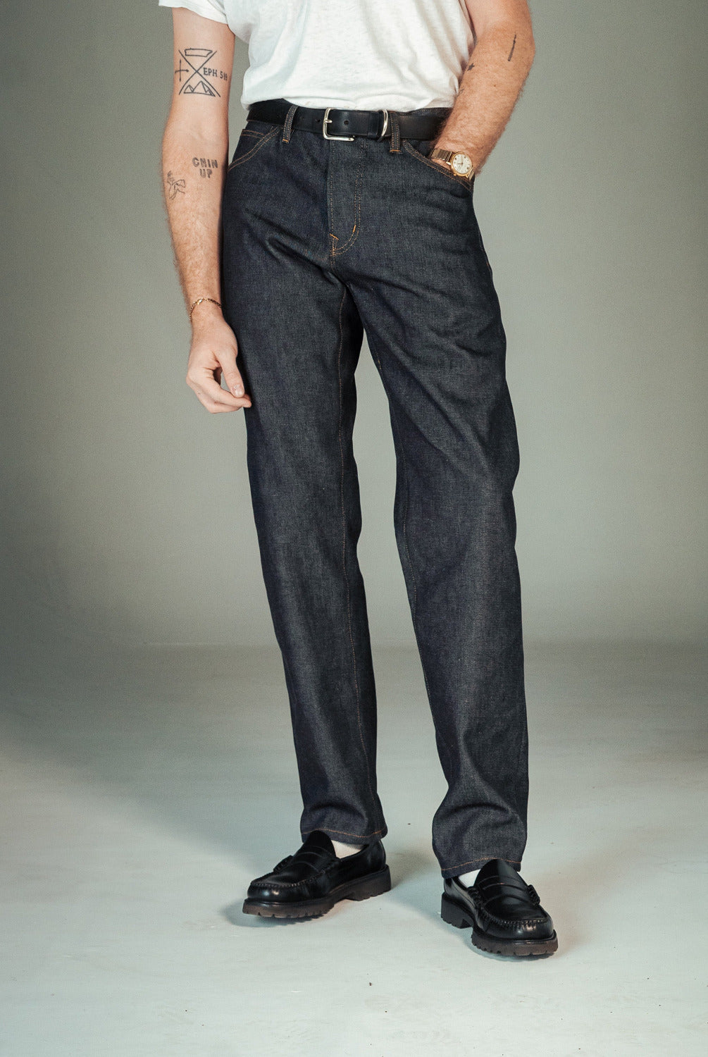 Person wearing dark jeans and black shoes on a plain background