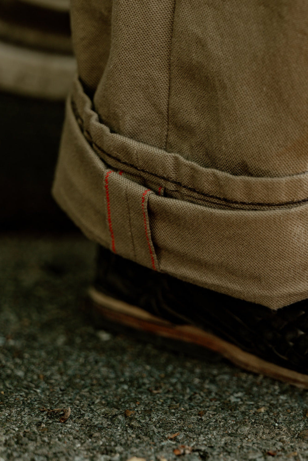 Close-up of a person wearing brown pants with rolled-up cuffs and a woven sandal on a concrete surface.